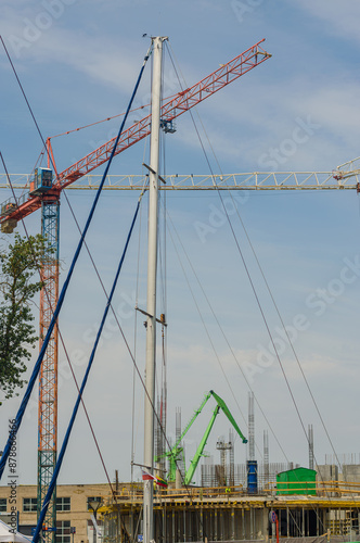 Construction cranes and white mast against the blue sky background. High quality photo