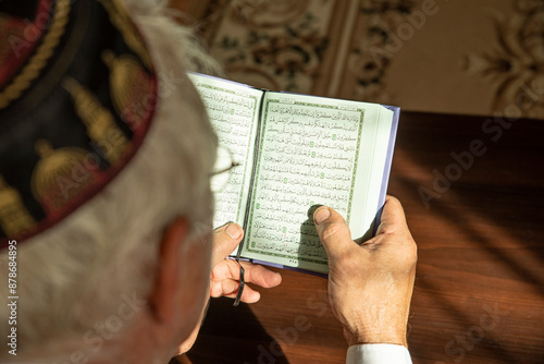 Lifestyle portrait of senior islamic man reading Quran at home. Natural aesthetic light photo