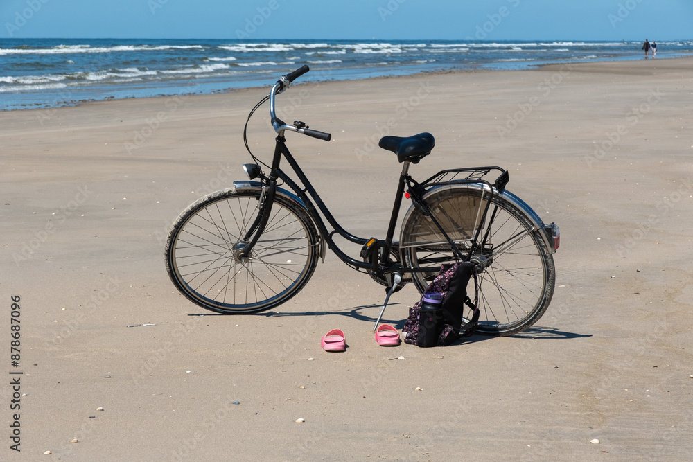 Fototapeta premium Ein schwarzes Fahrrad steht am Strand, Schuhe und ein Rucksack stehen davor 