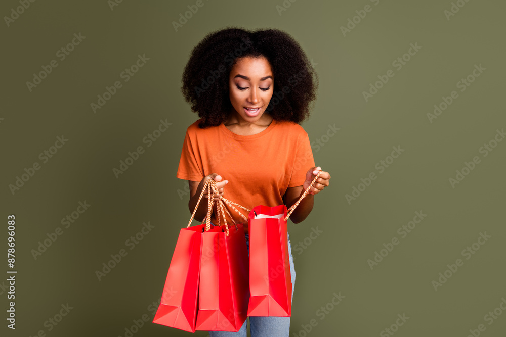 Photo of charming positive woman wear orange t-shirt open shoppers empty space isolated khaki color background Photo of charming positive woman wear orange t-shirt open shoppers empty space isolated khaki color background