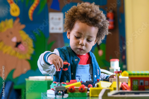 Toddler playing with a train set at nursery, kinder garden. Multi ethnic boy at playtime.  Colourful vibrant image.