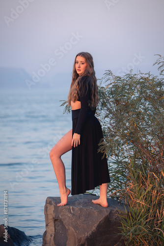 Young woman dancing in nature with water in the background.