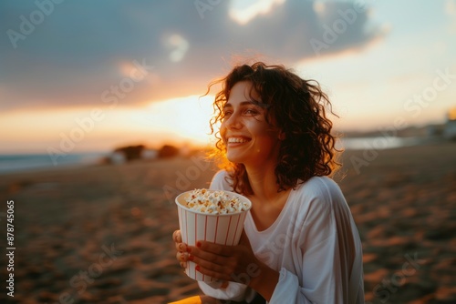 Carefree woman watching sunset on beach with popcorn in hand photo