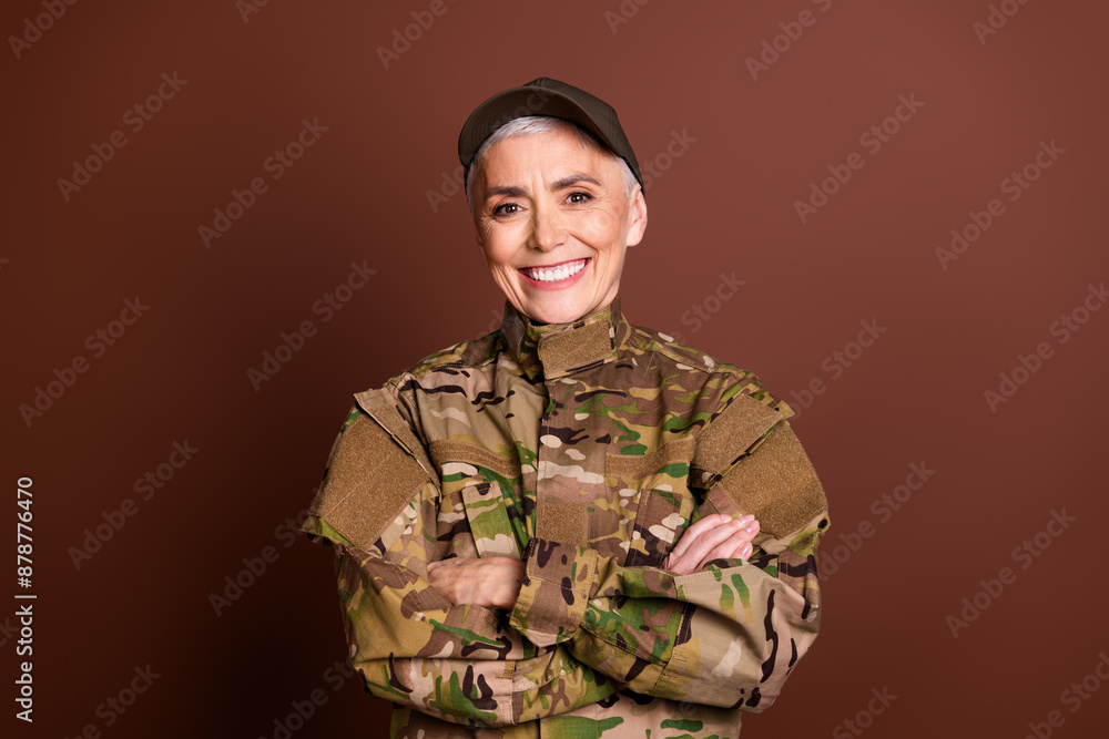 Photo of cheerful positive elderly lady dressed camo uniform arms folded empty space isolated brown color background Photo of cheerful positive elderly lady dressed camo uniform arms folded empty space isolated brown color background
