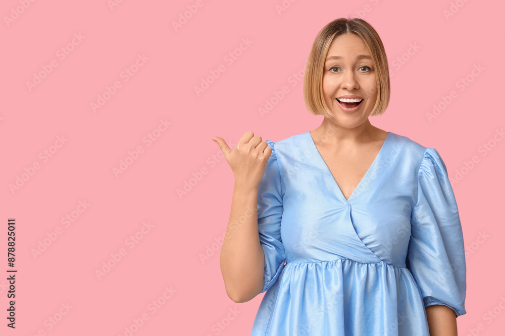 Surprised adult woman pointing at something on pink background Surprised adult woman pointing at something on pink background