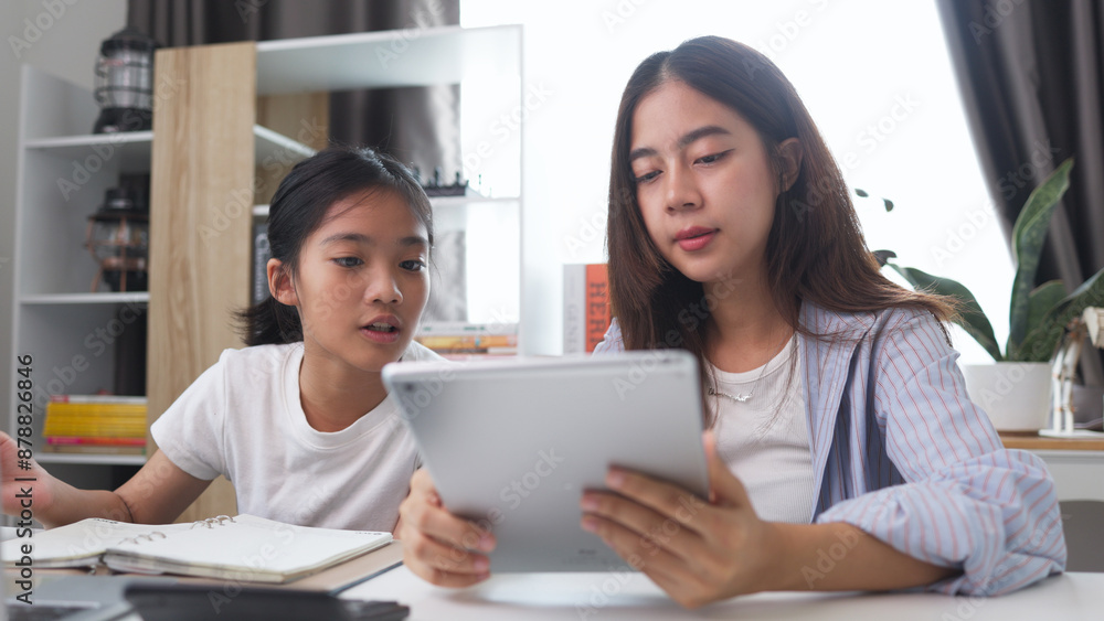 Asian siblings doing homework on a table at home Asian siblings doing homework on a table at home