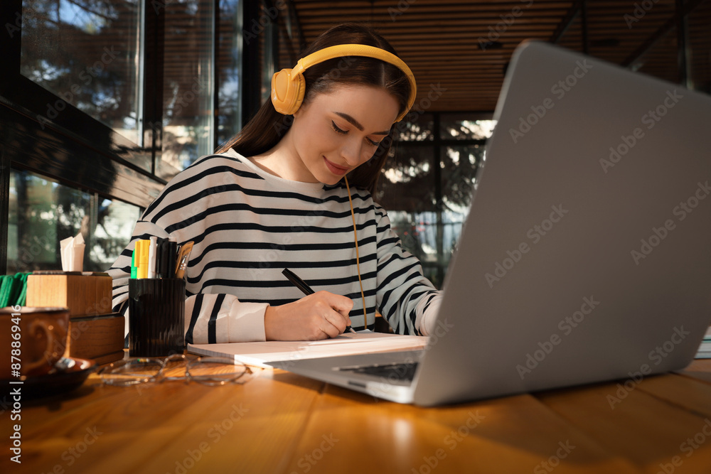 Young female student with laptop and headphones studying at table in cafe Young female student with laptop and headphones studying at table in cafe
