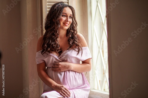 Portrait of a beautiful pregnant woman in pink dress at home.