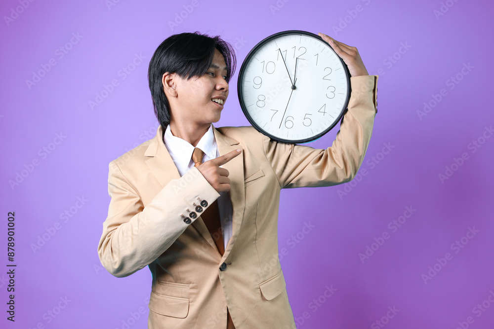 Friendly Young Asian Businessman Pointing And Holding Clock Isolated On Purple Background
Friendly Young Asian Businessman Pointing And Holding Clock Isolated On Purple Background
