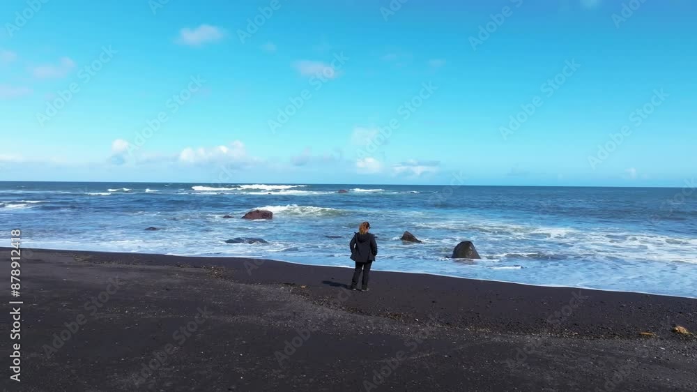 Blonde woman stares at the sea alone in volcanic Sao Miguel Azores beach drone aerial shot Blonde woman stares at the sea alone in volcanic Sao Miguel Azores beach drone aerial shot