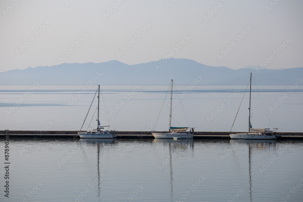three white boats with masts docked in the harbor on a calm sea three white boats with masts docked in the harbor on a calm sea