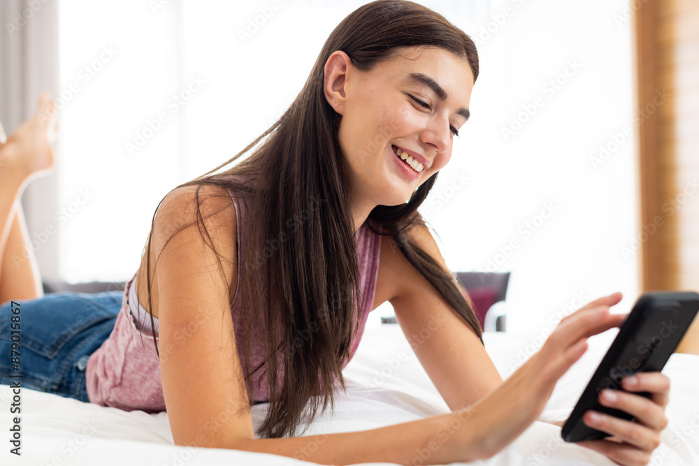 Teenage Caucasian girl lying on a bed at home, smiling at her phone Teenage Caucasian girl lying on a bed at home, smiling at her phone