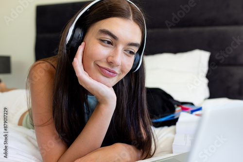 Teenage Caucasian girl enjoys music while studying at home photo