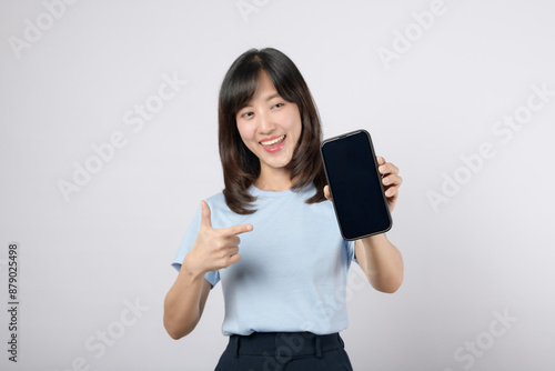 Smartphone application. young asian woman happy smile showing smartphone screen with pointing finger hand gesture to mobile phone isolated on white background. Blank screen smartphone concept.