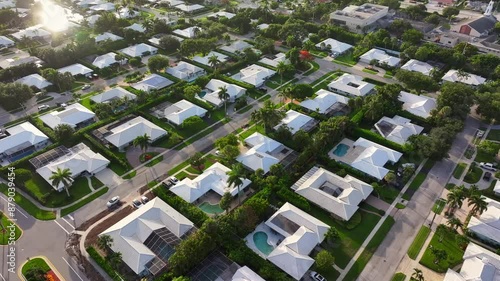 Expansive residential homes in a gated golf community in South Florida. American dream. Florida real estate development. Golden hour light drone shot. White roofs, green lawns and palm trees.