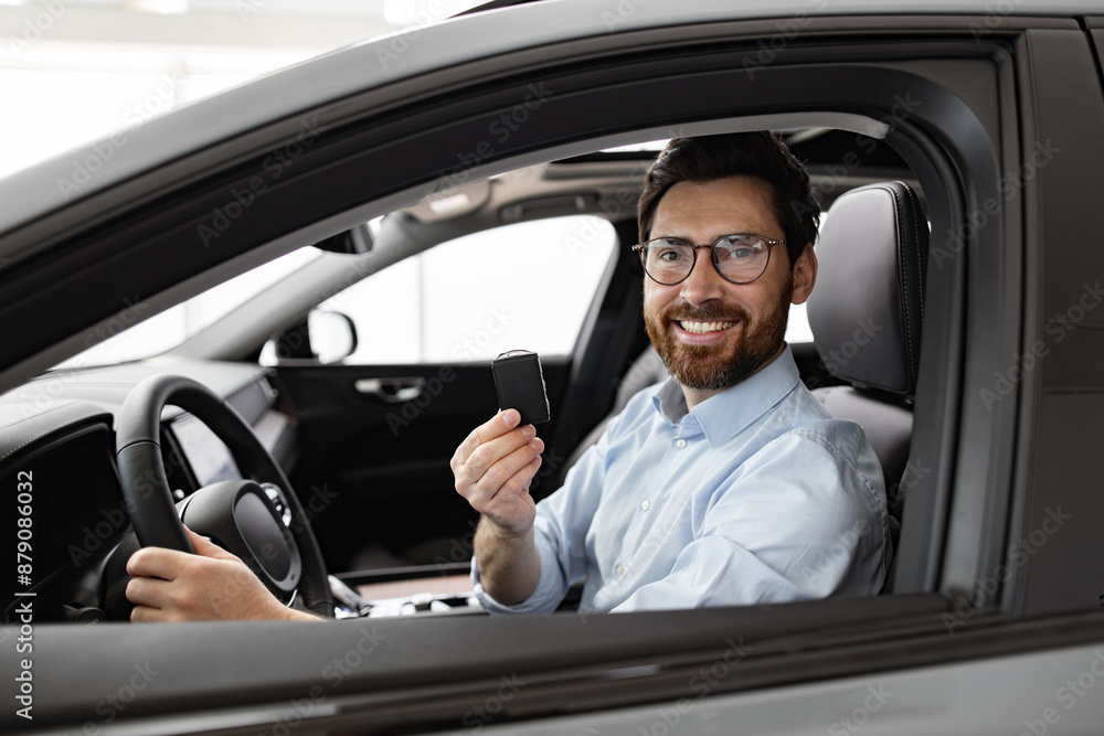 Businessman sitting inside vehicle holding car key at dealership. Smiling confidently, wearing glasses and formal shirt. New car purchase or sales concept, showcasing success, professionalism. Businessman sitting inside vehicle holding car key at dealership. Smiling confidently, wearing glasses and formal shirt. New car purchase or sales concept, showcasing success, professionalism.
