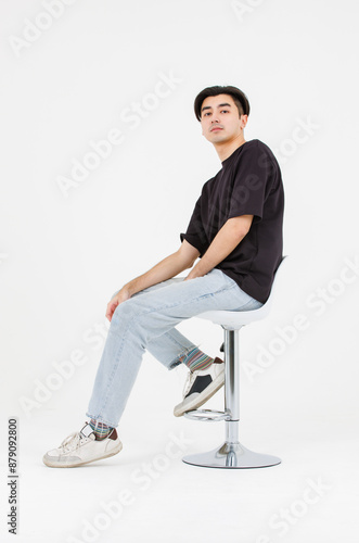 Portrait of asian male confidence charming successful handsome young guy , Wearing black t-shirt and jeans posing relaxed looking attractive sitting on chair in white background studio - isolated