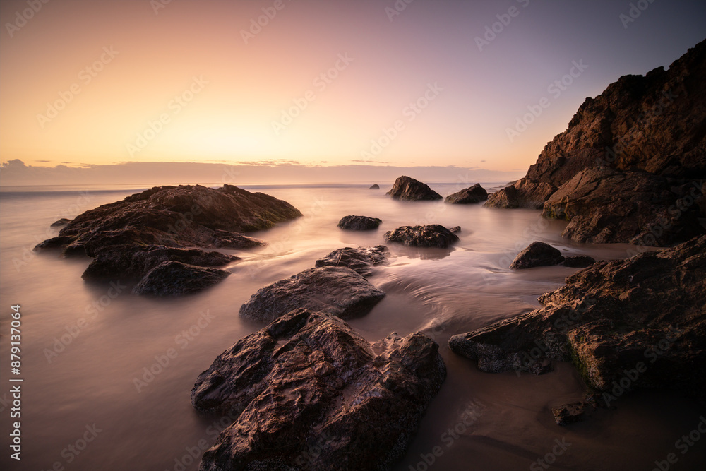 Rocky shore at Sunrise with smooth, silky water and warm light Rocky shore at Sunrise with smooth, silky water and warm light