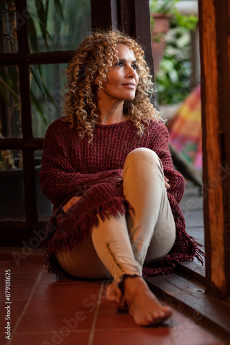 Relax and indoor leisure activity with one woman alone sitting on the floor smiling serene and looking outside the door. Female people enjoying happy lifestyle and positive thinking. Pretty lady photo