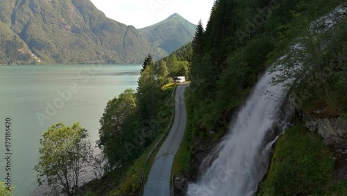 A beautiful and tranquil lake surrounded by lush mountains, meandering road, and a magnificent waterfall. Fjaerlandsfjorden, Fjord, Vestland, Norway photo