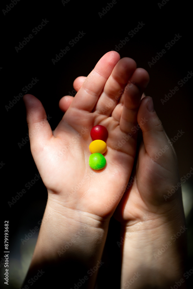 small round candies of red, yellow, green color in the hands of a child in close-up. small round candies of red, yellow, green color in the hands of a child in close-up.