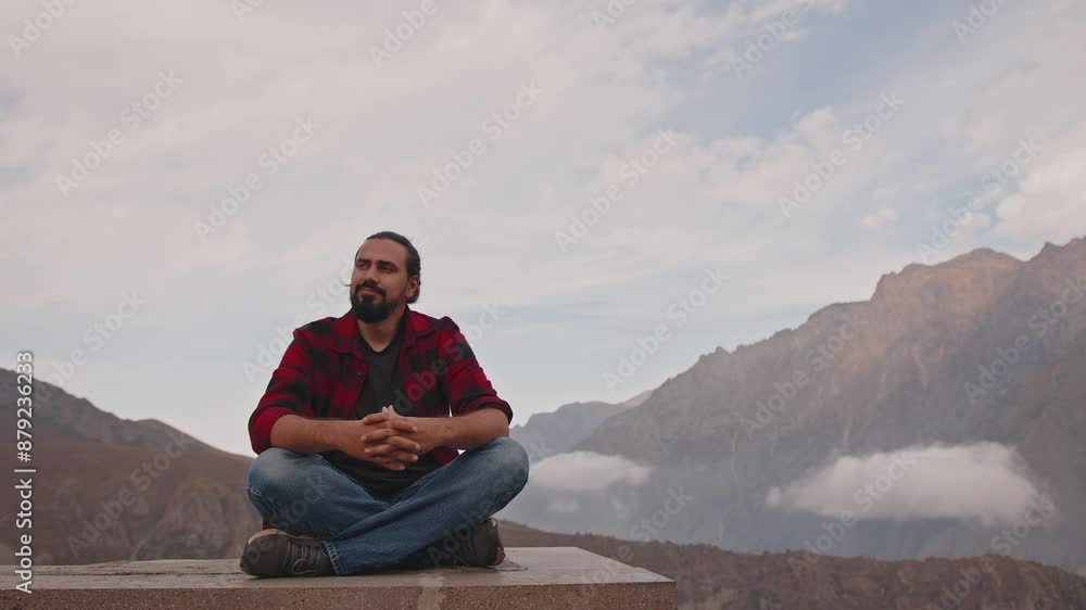 A Caucasian man sits on the edge of a cliff enjoying the mountain landscape A Caucasian man sits on the edge of a cliff enjoying the mountain landscape