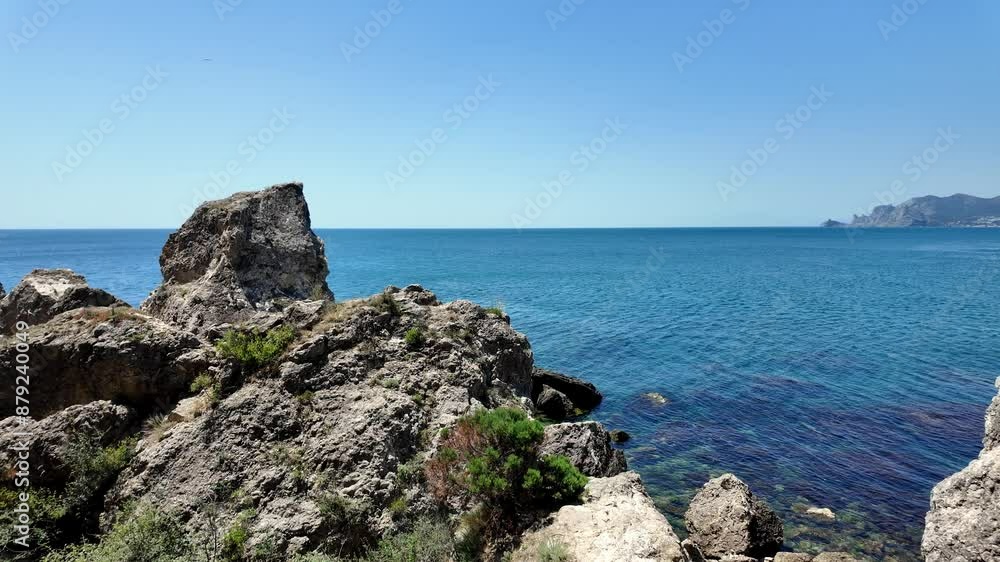 A picturesque view of the Black Sea from a rocky cliff in Sudak, Crimea, Russia. The water is clear and blue, and the sky is a beautiful light blue. A picturesque view of the Black Sea from a rocky cliff in Sudak, Crimea, Russia. The water is clear and blue, and the sky is a beautiful light blue.