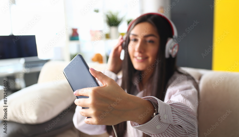 Young beautiful woman headphones holds smartphone in hand using at home costs about sofa. makes selfie internal information financial advertising freedom makes money level transfer contractor concept Young beautiful woman headphones holds smartphone in hand using at home costs about sofa. makes selfie internal information financial advertising freedom makes money level transfer contractor concept