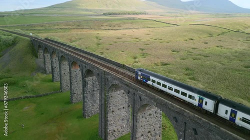 Passenger train crossing railway bridge over Northern English moorland at golden hour. Drone close flyover. Ribblehead Viaduct, North Yorkshire, England, UK photo