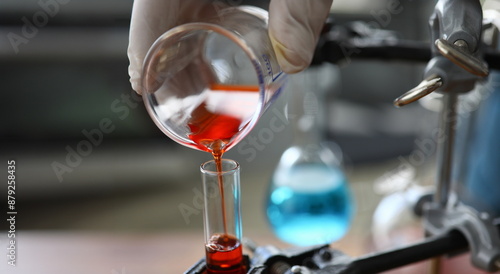 Focus on male hand in sterile gloves holding bulb. Pharmaceutist transfusing red fluid in glass flask. Medicine experiments and researches concept. Blurred background photo