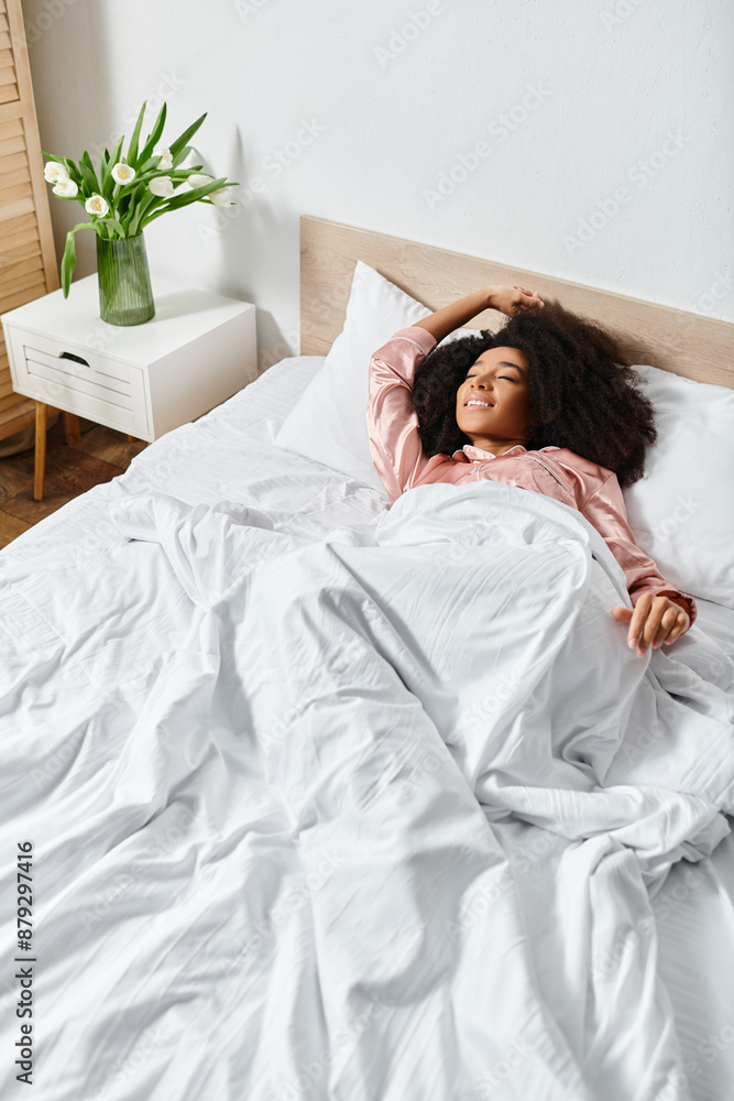 Curly African American woman in pajamas lying on a bed with white sheets, enjoying a peaceful morning. Curly African American woman in pajamas lying on a bed with white sheets, enjoying a peaceful morning.