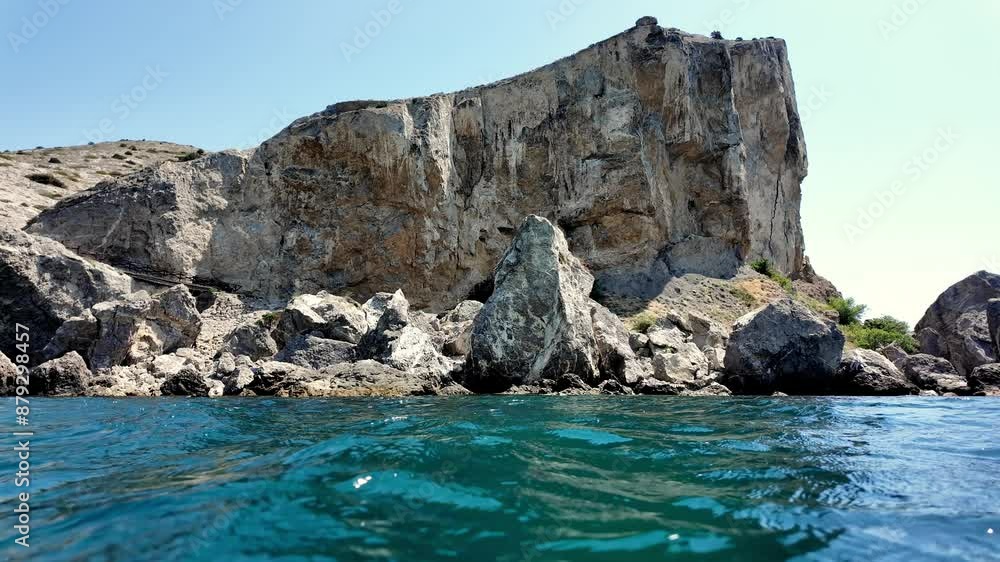 The iconic Sudak Fortress cliff in Crimea, Russia, viewed from the water's surface, showcasing the towering rock formations and crystal clear waters. The iconic Sudak Fortress cliff in Crimea, Russia, viewed from the water's surface, showcasing the towering rock formations and crystal clear waters.