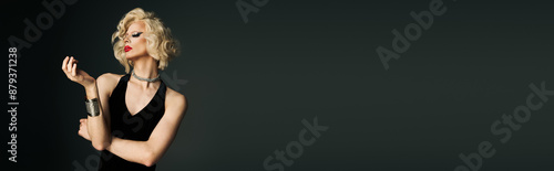Konstfotografi A drag queen with dramatic makeup and a blonde wig poses in a black dress against a dark background