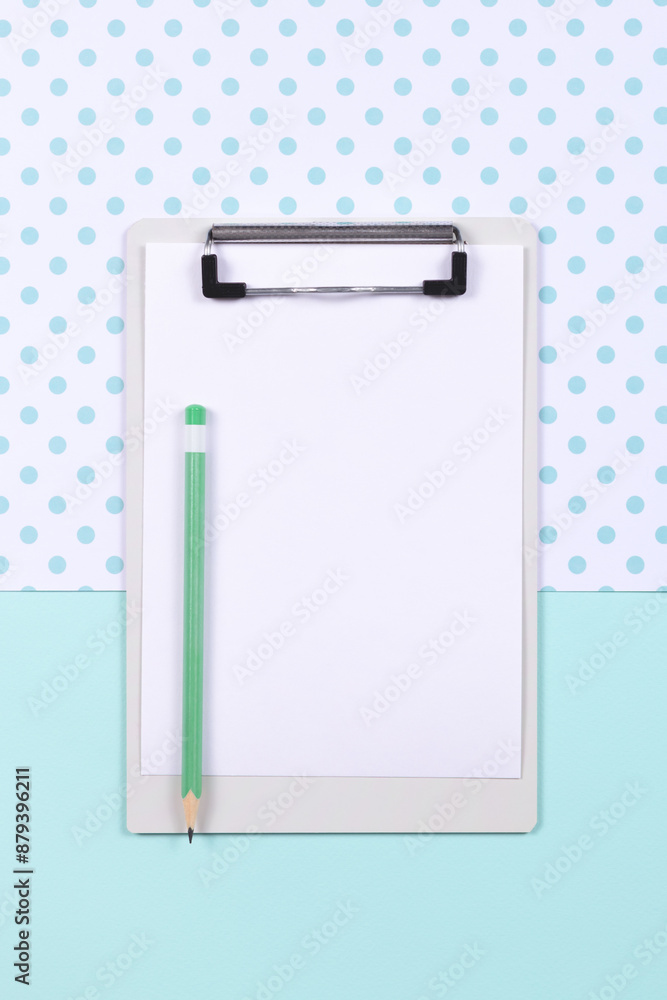 Top view of clipboard with empty white page and green pencil on two color blue and white background. Copy space. Top view of clipboard with empty white page and green pencil on two color blue and white background. Copy space.