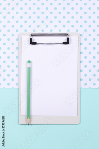 Top view of clipboard with empty white page and green pencil on two color blue and white background. Copy space.