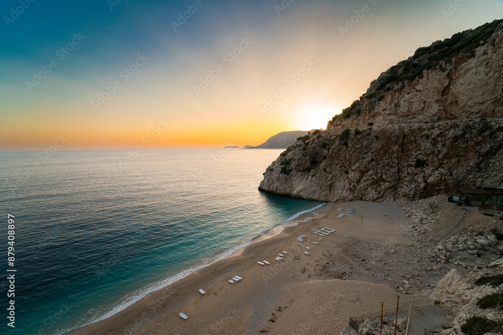 Fototapeta premium Kaputas beach. People enjoying the sun and the sea on the turquoise sea and sandy beach of Kaputaş. Sunset over the sea in the background. Mediterrenian.
