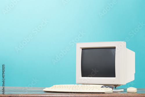 Retro desktop computer monitor, keyboard and mouse from circa 90s on oak wooden table front mint blue background. Vintage style filtered photo