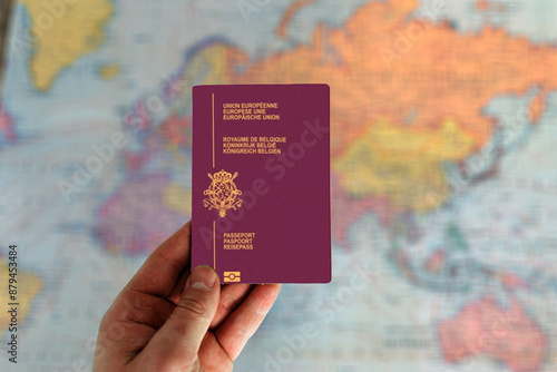 Man holding Belgium passport in hand and world map in background