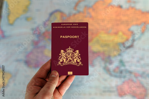 Man holding Netherlands passport in hand and world map in background