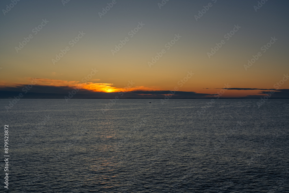 Obraz premium A small solitary fishing boat sails across the calm waters of the Skagerrak Sea, with the rising sun casting a golden glow on the horizon near the coast of Norway