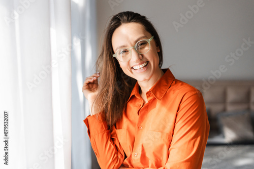 Smiling woman in eyeglasses looking at camera while posing at home