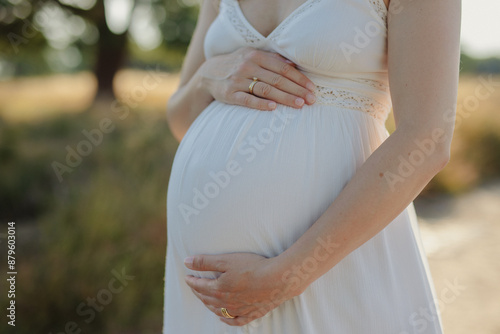 pregnant woman holding her baby belly in a white dress photo