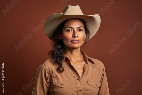 Portrait of a glad indian woman in her 30s wearing a rugged cowboy hat on solid color backdrop © Markus Schröder