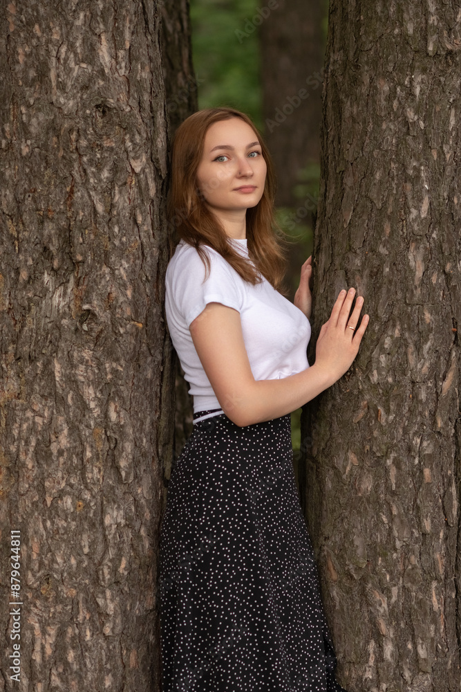 Portrait of a beautiful long-haired girl in a white T-shirt and black skirt in a city park. Portrait of a beautiful long-haired girl in a white T-shirt and black skirt in a city park.