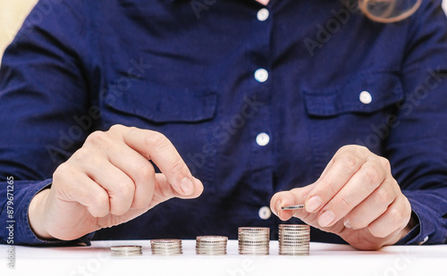 Woman stacks coins on white table, dark clothes