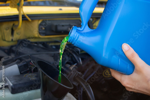 Pouring coolant antifreeze fluid into reservoir in vehicle engine using black funnel photo