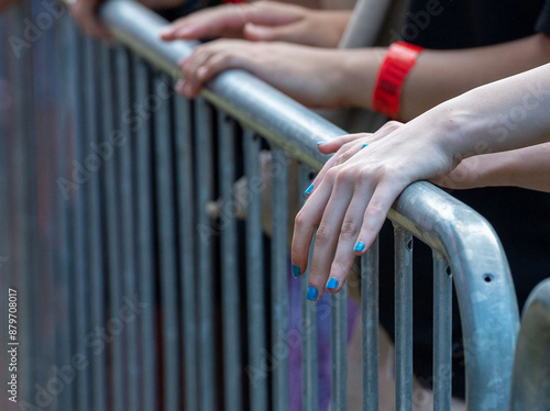 Close-Up Shot of Hands with Blue Varnished Nails on Metal Fence: People in Front of the Stage.