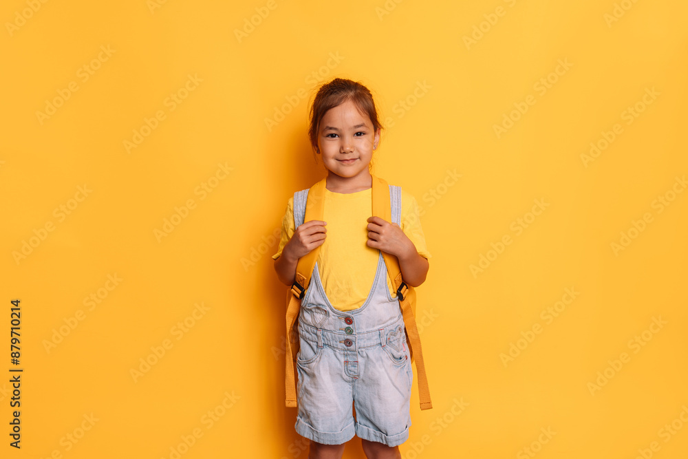 A girl with a backpack stands in front of a yellow background. A girl with a backpack stands in front of a yellow background.