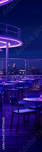 An outdoor rooftop dining area at night, lit with purple lights. Tables and chairs are visible.