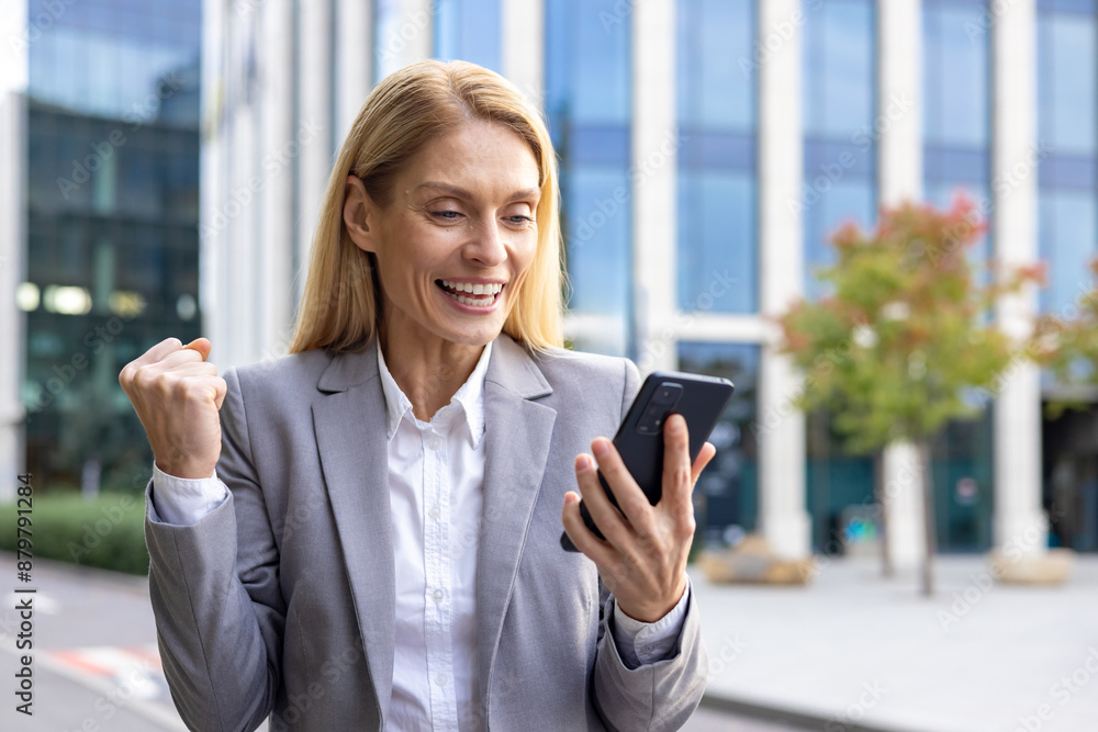 Businesswoman celebrating success while looking at her mobile phone. Joyful moment outdoors in modern city area. Concept of achievement, communication, and professional success. Businesswoman celebrating success while looking at her mobile phone. Joyful moment outdoors in modern city area. Concept of achievement, communication, and professional success.
